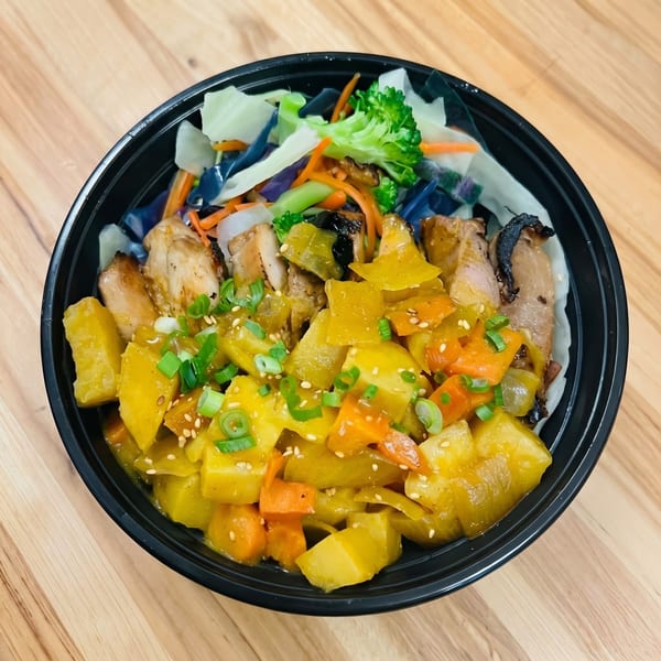 A black bowl filled with chicken, yellow curry, carrots, broccoli, and cabbage on a wooden table.
