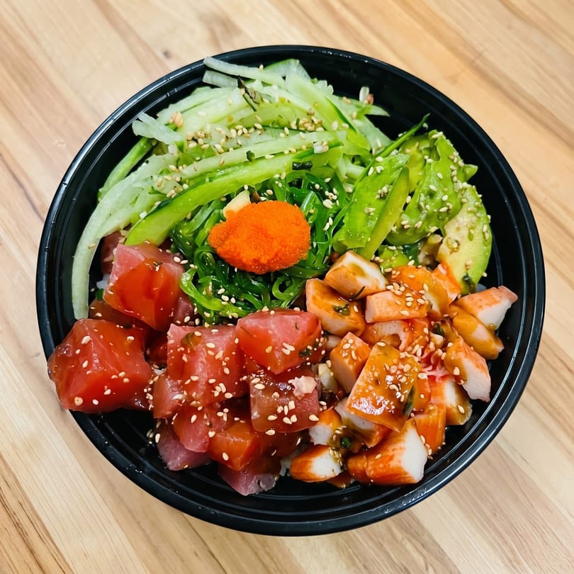 A vibrant poke bowl with tuna, crab, avocado, seaweed salad, cucumber, and roe.